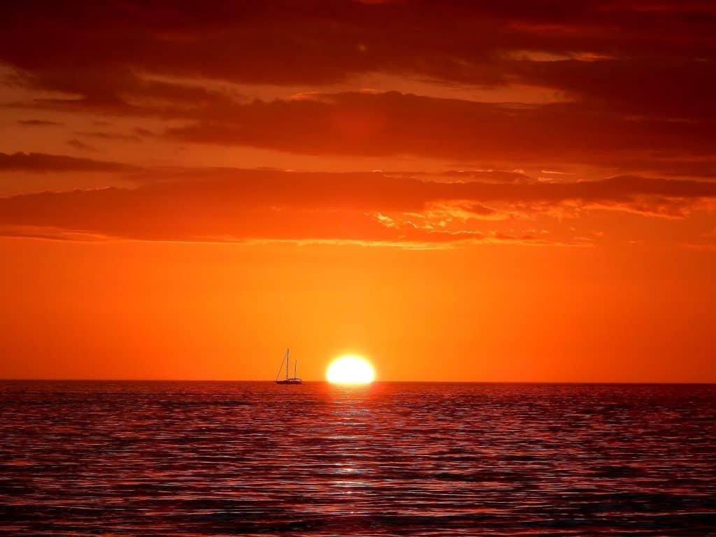 An ocean sunset with the silhouette of a boat on the horizon